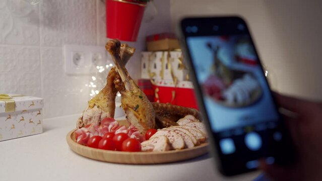woman takes photos on her phone of carved roasted turkey with tomatoes and bacon on wooden tray. Thanksgiving and christmas holiday dinner
