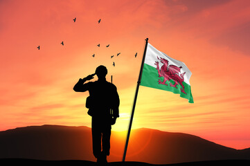 Silhouette of a soldier with the Wales flag stands against the background of a sunset or sunrise....