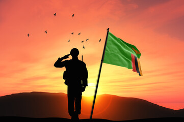 Silhouette of a soldier with the Zambia flag stands against the background of a sunset or sunrise....