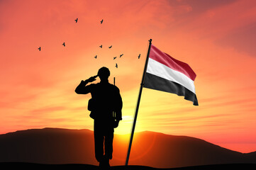 Silhouette of a soldier with the Yemen flag stands against the background of a sunset or sunrise....