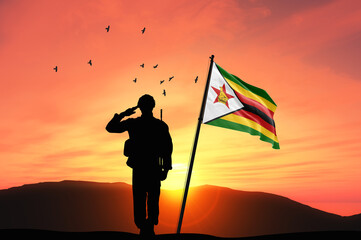 Silhouette of a soldier with the Zimbabwe flag stands against the background of a sunset or...