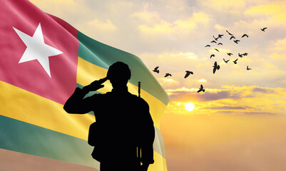 Silhouette of a soldier with the Togo flag stands against the background of a sunset or sunrise....