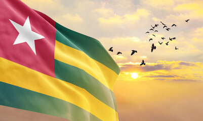 Waving flag of Togo against the background of a sunset or sunrise. Togo flag for Independence Day....