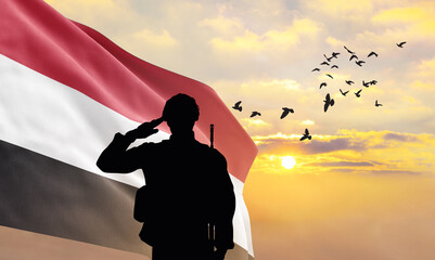 Silhouette of a soldier with the Yemen flag stands against the background of a sunset or sunrise. Concept of national holidays. Commemoration Day. - obrazy, fototapety, plakaty