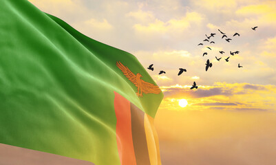 Waving flag of Zambia against the background of a sunset or sunrise. Zambia flag for Independence Day. The symbol of the state on wavy fabric. - obrazy, fototapety, plakaty