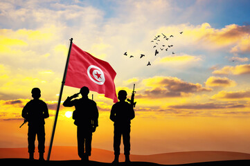 Silhouettes of soldiers with the Tunisia flag stand against the background of a sunset or sunrise....