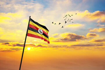 Waving flag of Uganda against the background of a sunset or sunrise. Uganda flag for Independence...