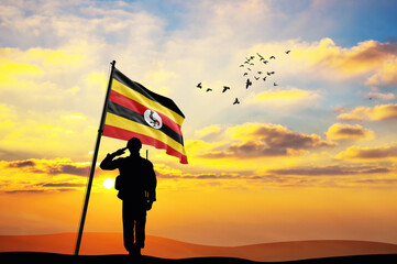 Silhouette of a soldier with the Uganda flag stands against the background of a sunset or sunrise....