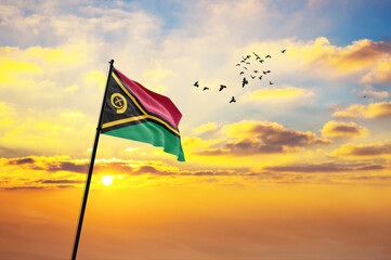 Waving flag of Vanuatu against the background of a sunset or sunrise. Vanuatu flag for Independence Day. The symbol of the state on wavy fabric.