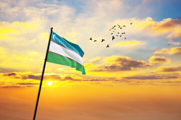 Waving flag of Uzbekistan against the background of a sunset or sunrise. Uzbekistan flag for...