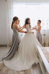 Friends rejoice with the bride in the morning. They take pictures, smile, help the bride fasten her dress. - obrazy, fototapety, plakaty