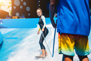 Beautiful young woman surfing with trainer on a wave simulator at a water amusement park