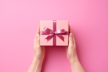 Woman hand holding a gift box on pink background. Valentine's day background. Top view, copy space.