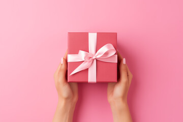Woman hand holding a gift box on pink background. Valentine's day background. Top view, copy space.