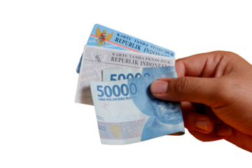 A man's hand is holding a photocopy of his KTP and a 50,000 rupiah note. concept illustration of buying or bribing election votes