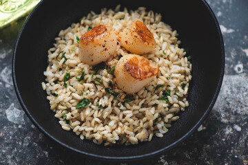 Seared scallops served with brown rice, lemon zest and parsley in a black bowl, horizontal shot, middle closeup