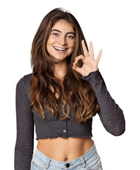 Young Caucasian woman in studio setting cheerful and confident showing ok gesture.