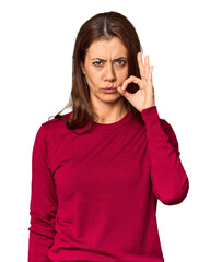 Elegant middle-aged Caucasian woman in studio setting with fingers on lips keeping a secret.