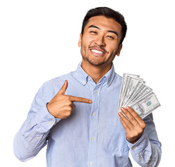 Young Chinese man holding dollar bills in studio person pointing by hand to a shirt copy space,...