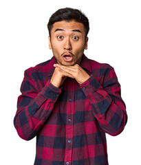 Young Chinese man in studio background praying for luck, amazed and opening mouth looking to front.