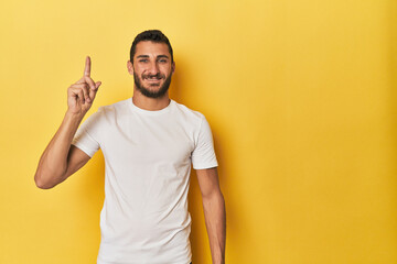 Young Hispanic man on yellow background showing number one with finger.
