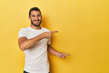 Young Hispanic man on yellow background pointing with forefingers to a copy space, expressing...