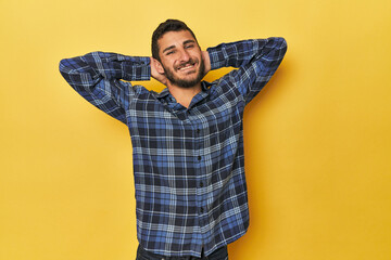 Young Hispanic man on yellow background stretching arms, relaxed position.