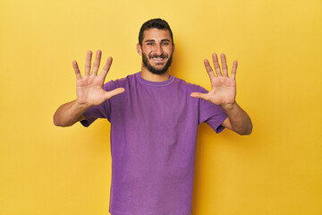 Young Hispanic man on yellow background showing number ten with hands.