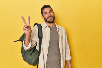 Young Hispanic man with travel backpack joyful and carefree showing a peace symbol with fingers.