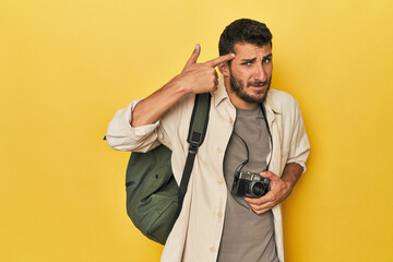 Young Hispanic travel photographer poses showing a disappointment gesture with forefinger.