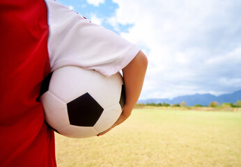Child, arm and soccer ball on green grass for sports, training or practice in cloudy blue sky....