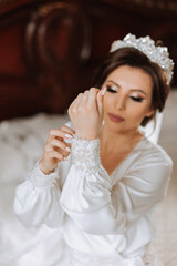 Obraz na płótnie Canvas A beautiful brunette bride with a tiara in her hair is getting ready for the wedding in a beautiful robe in boudoir style. Close-up wedding portrait, photo.