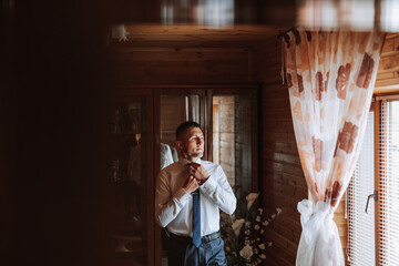 A stylish groom is tying his tie, preparing for the wedding ceremony. Groom's morning. A...