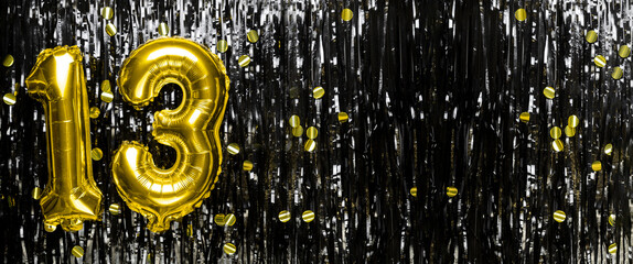 Gold foil balloon number number 13 on a background of black tinsel decoration. Birthday greeting...