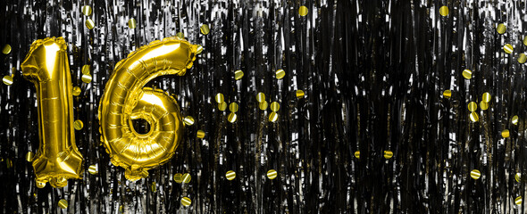 Gold foil balloon number number 16 on a background of black tinsel decoration. Birthday greeting...