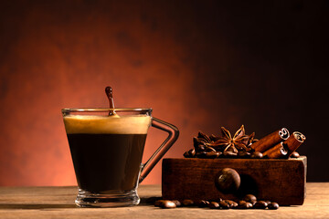 front view, in the foreground a glass cup with espresso and gush, aside from coffee beans, star anise and cinnamon sticks