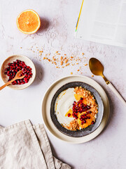Müsli mit Joghurt und Obst in einer Schüssel und eine Zeitung auf einem grauen Tisch. Gesundes Frühstück.