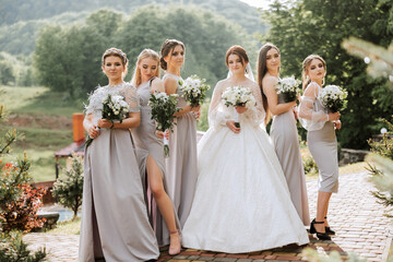 Group portrait of the bride and bridesmaids. A bride in a wedding dress and bridesmaids in silver dresses hold stylish bouquets on their wedding day. - Powered by Adobe