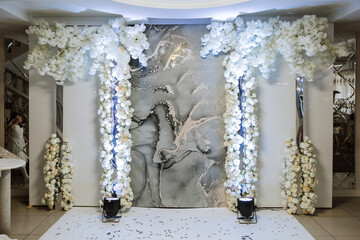 A beautifully decorated place for the wedding ceremony of the bride and groom in a modern style. Wedding arch made of white fresh flowers. Beautiful decorative candles.