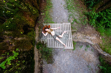 top view of sexy, young, red-haired woman lies like dead on a concrete bridge of a forest path on a...