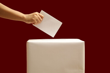 hand inserting ballot paper into election box on plain red background