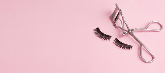 Flat lay composition of curler and false eyelashes on pink background, space for text, banner