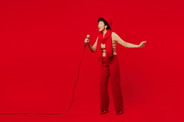 Full body young fun woman of African American ethnicity she wears beige sweater hat scarf sing song in microphone at karaoke club isolated on plain red background studio portrait. Lifestyle concept.