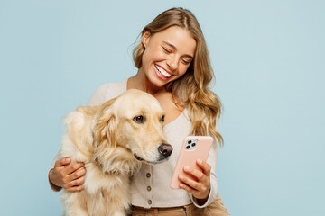 Young smiling owner woman with her best friend retriever wear casual clothes use mobile cell phone hug embrace dog isolated on plain pastel light blue background studio. Take care about pet concept.