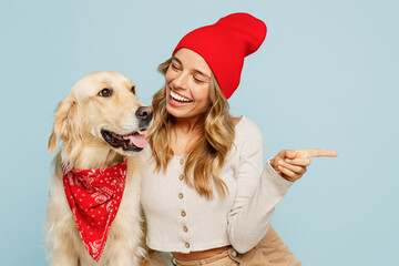 Young owner woman with her best friend retriever dog wears casual clothes red hat bandana point index finger aside on area isolated on plain pastel blue background studio. Take care about pet concept.
