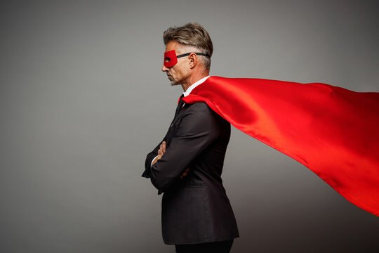 Sideways adult cool successful employee business man corporate lawyer wears classic formal black suit shirt tie super hero red cloak work in office isolated on plain grey background studio portrait.