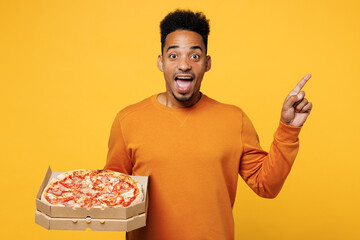 Young amazed man wear casual clothes hold italian pizza in cardboard flatbox point finger aside on...