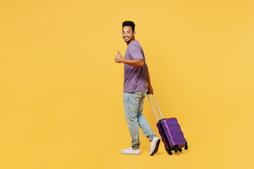Traveler man wears summer casual clothes hold bag show thumb up walk isolated on plain yellow background studio. Tourist travel abroad in free spare time rest getaway. Air flight trip journey concept.