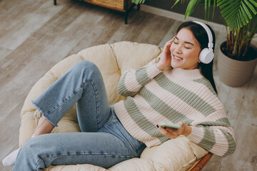 To view young woman wear casual clothes listen music in headphones use mobile cell phone sit on...