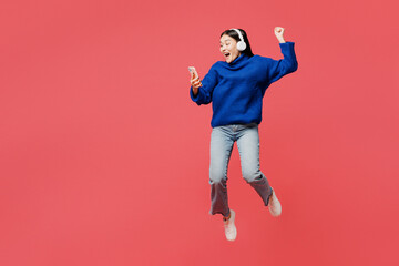 Full body young winner woman of Asian ethnicity she wear blue sweater casual clothes jump high hold...